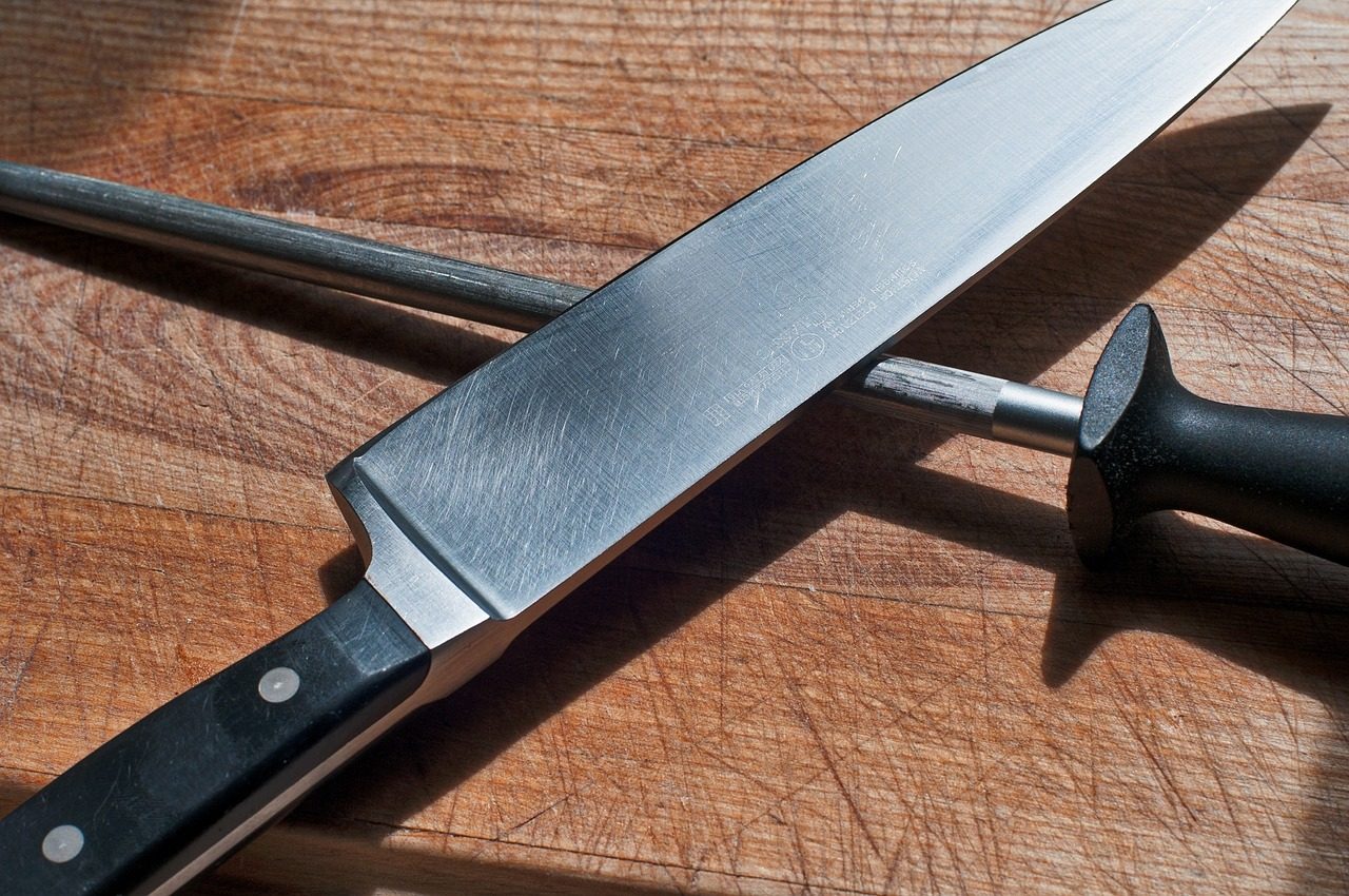 A chef's knife lying crosswise on a wooden cutting board beside a sharpening steel.