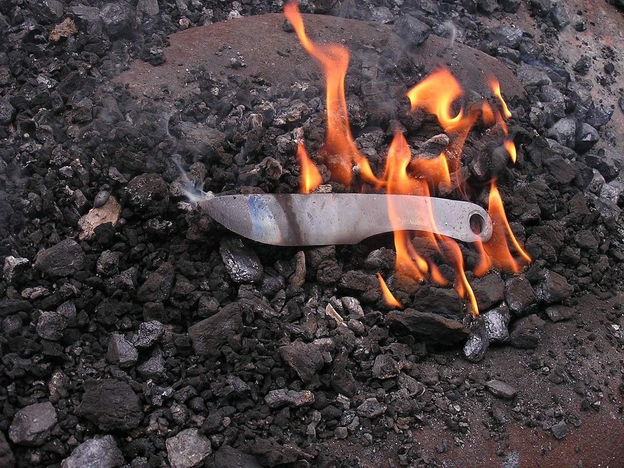 A knife blade lying on hot coals with flames rising beside it