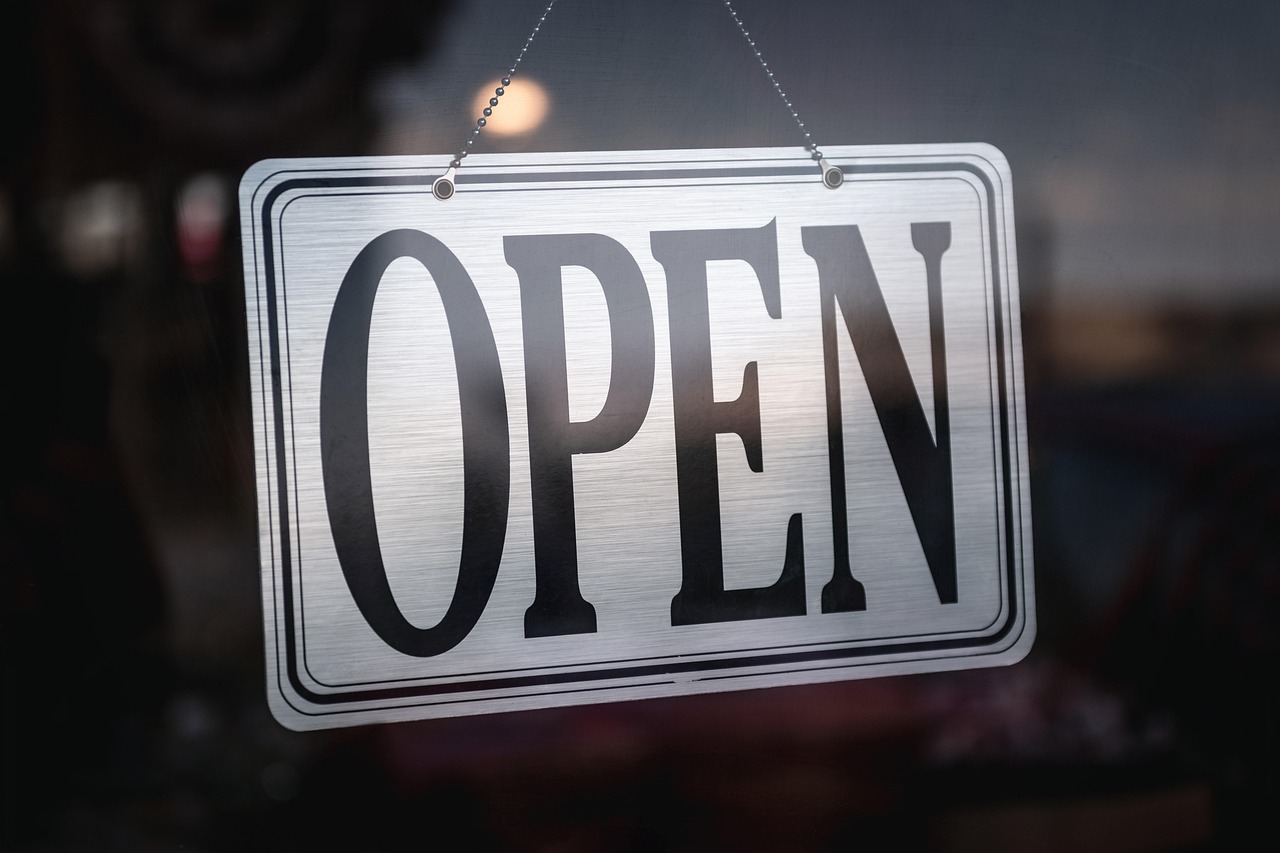 A metal OPEN sign hanging in a dark shop window.